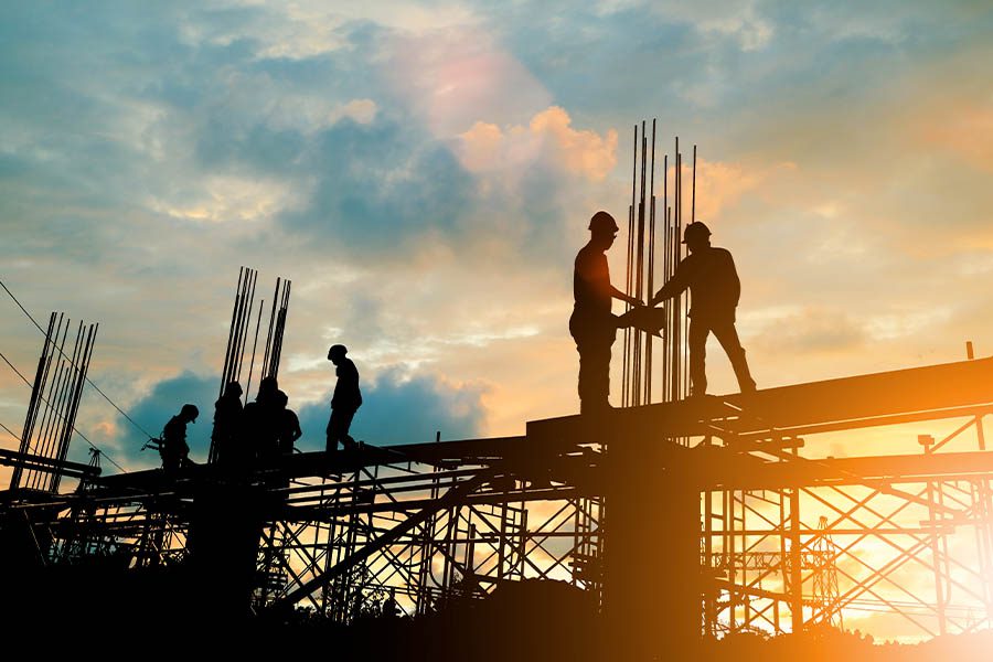 Workers’ Compensation Insurance - Silhouette of Engineer and Construction Team Working at Site Over Blurred Background Sunset